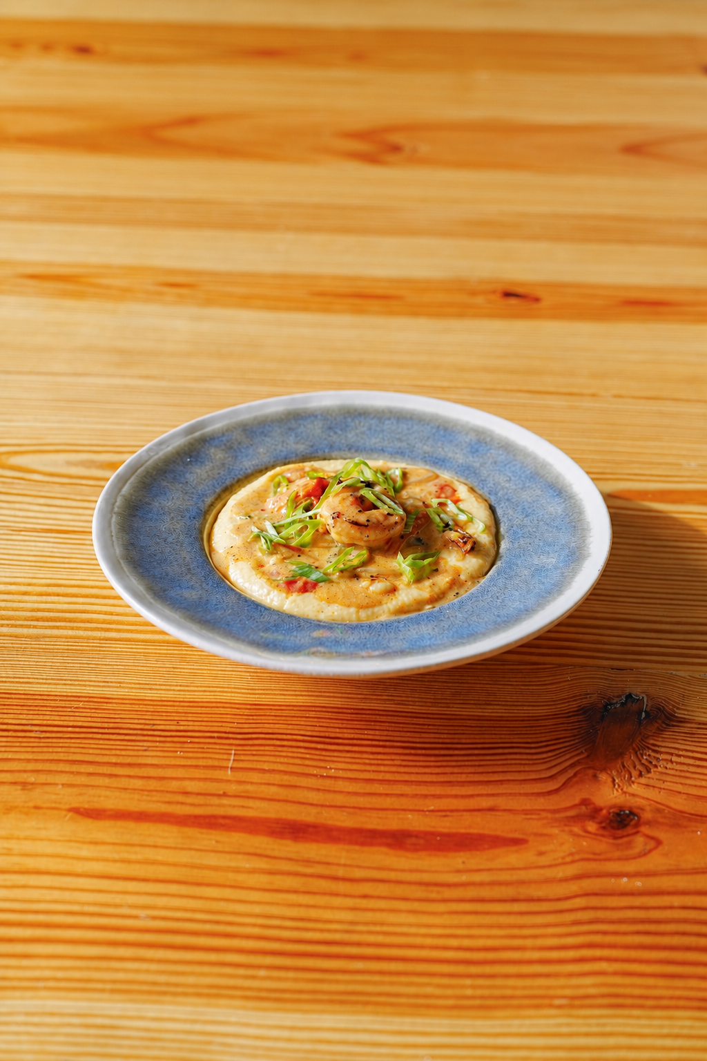 Shrimp and grits in a blue ceramic bowl on the Coffee Nutz wooden table